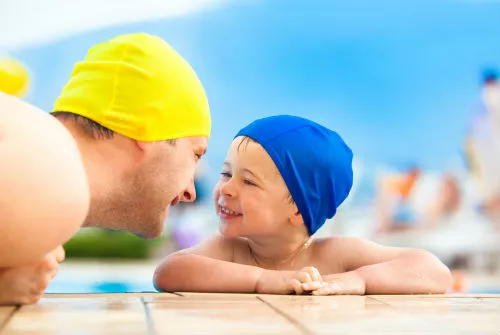 Father and son smiling while swimming in a pool